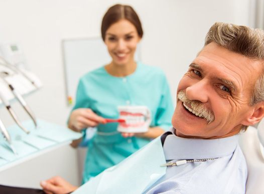 older man smiling in dental chair with hygienist 