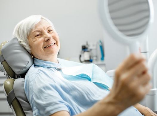 older woman admiring her smile in hand mirror 