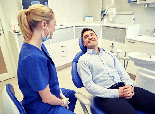 man sitting in dental chair and smiling at his dentist 