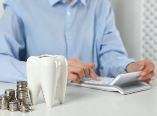 a man checking the cost of cosmetic dentistry next to a ceramic tooth and some coins