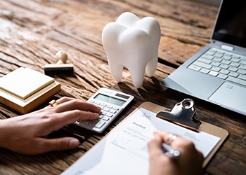 Person using calculator on desk next to laptop and prop tooth