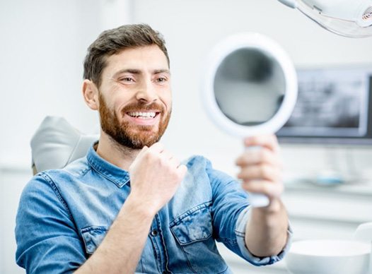 man admiring his smile in mirror after seeing cosmetic dentist in Moses Lake 