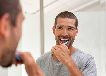 man brushing his teeth in front of a mirror