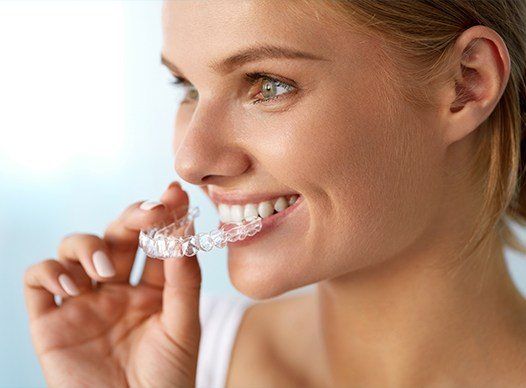 young woman holding invisalign in front of mouth