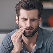 Man with beard holding his jaw in pain