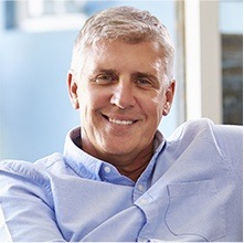 Man in light blue collared shirt smiling on couch