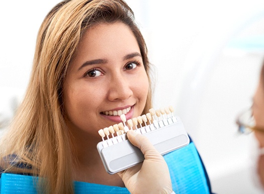 A young woman looking at the camera while a dentist uses a shade guide
