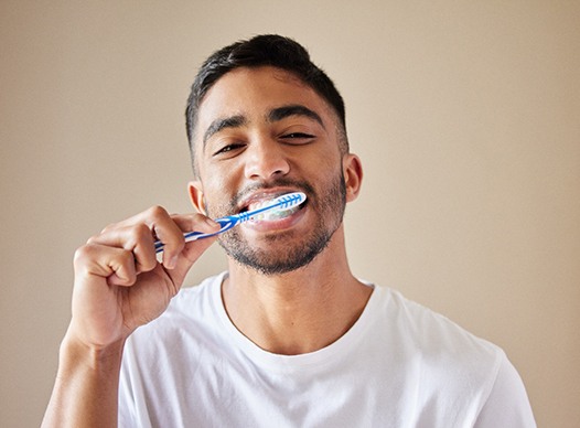 Man smiling while brushing his teeth