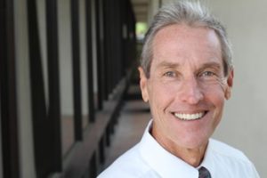 Man standing in a hallway smiling and wearing a white collared shirt