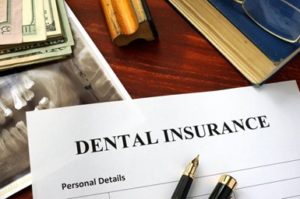 Dental insurance form sitting on a desk surrounded by a dental X-ray, a pen, a stack of money and an ink stamp.