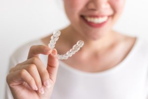 smiling woman holding an Invisalign aligner in Moses Lake 