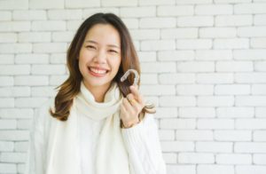a woman smiling while holding her Invisalign aligners