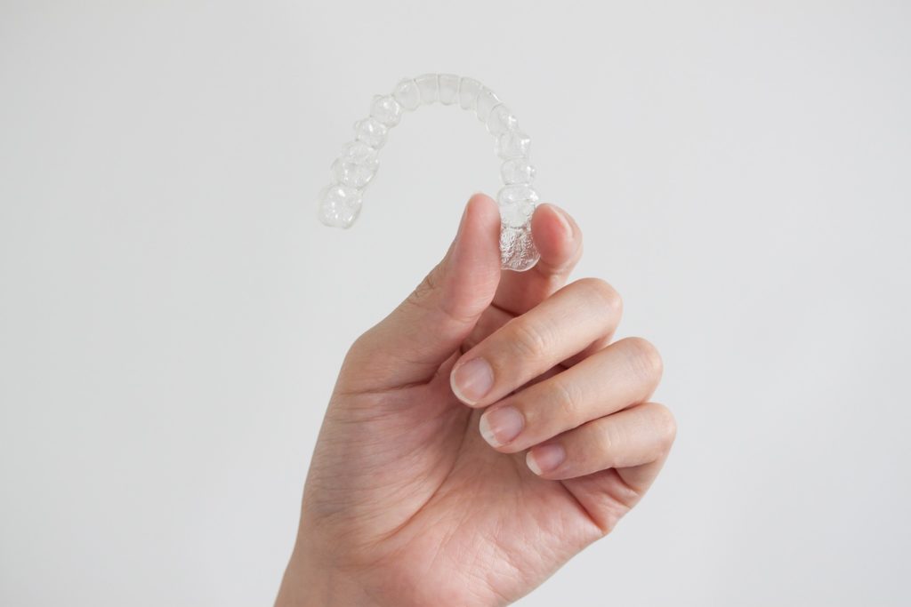 Closeup of person holding clear aligner against white background