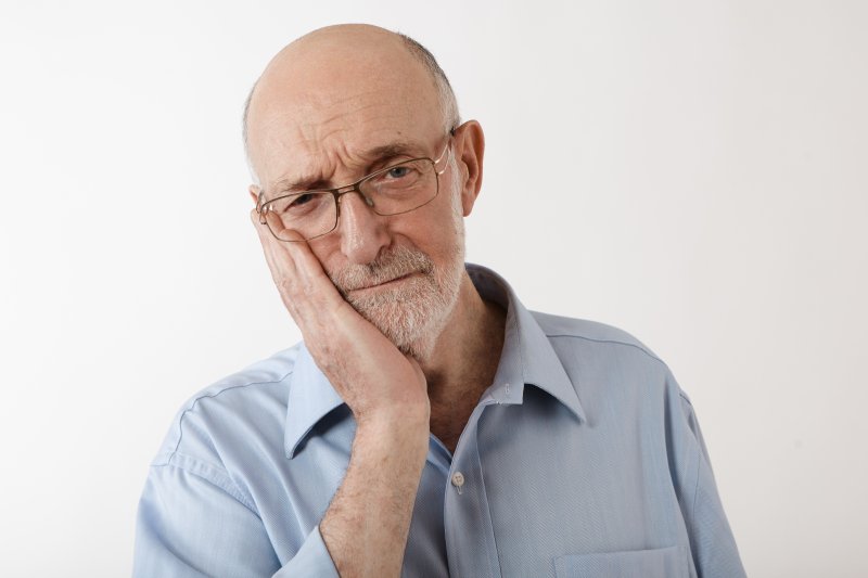 An older man holding his cheek due to denture sores