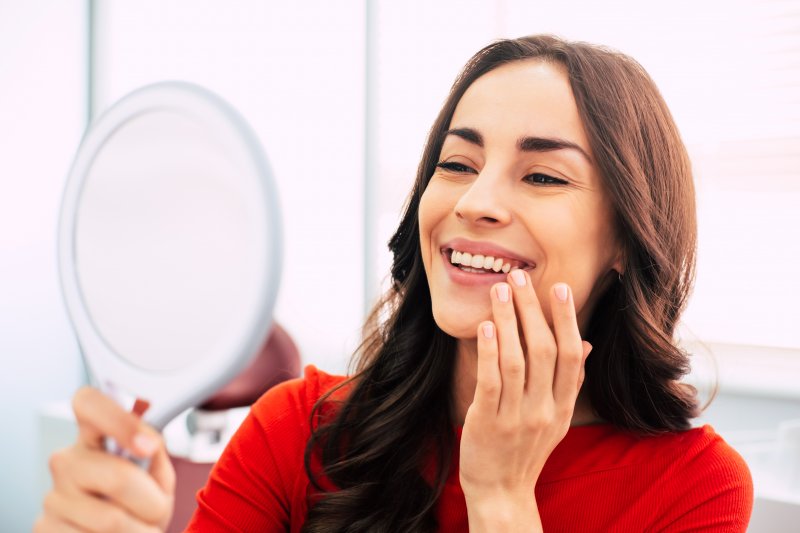 A woman smiling as she looks at her straightened teeth after Invisalign treatment